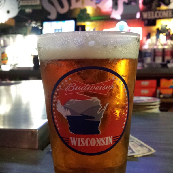 A glass of beer with a "Budweiser Wisconsin" label sits on a bar counter.