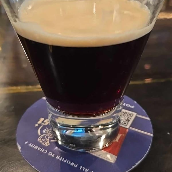 Dark drink with a creamy foam top in a martini glass on a blue coaster.