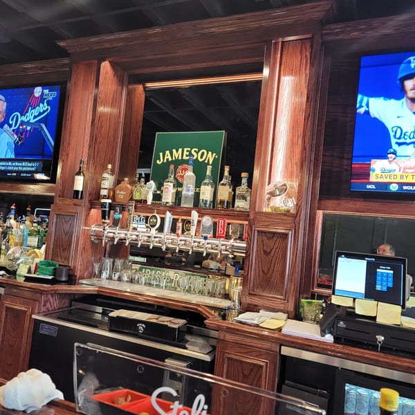 A well-stocked bar with a Jameson sign, beer taps, liquor bottles, and TVs showing sports.