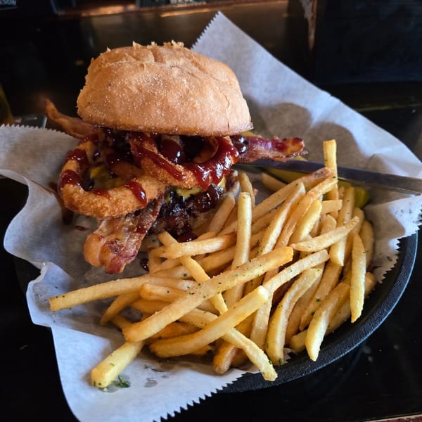 A BBQ bacon cheeseburger topped with onion rings and a side of golden french fries.